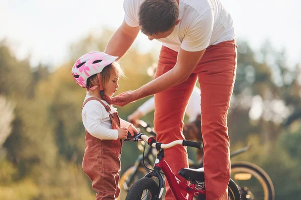 Beautiful sunlight. Father in white shirt teaching daughter how to ride bicycle outdoors.
