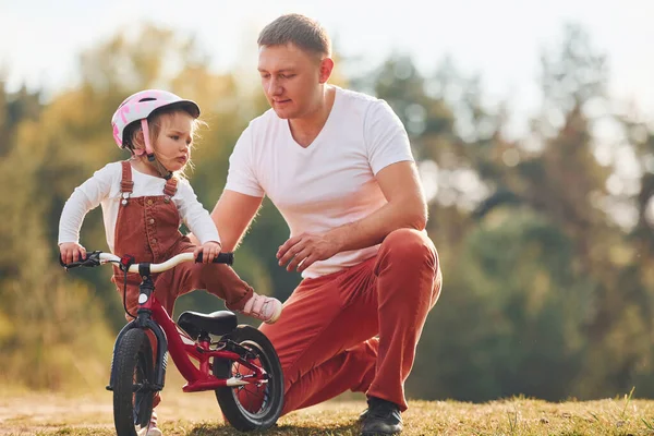 Güzel güneş ışığı. Beyaz gömlekli baba kızına dışarıda bisiklet sürmeyi öğretiyor..