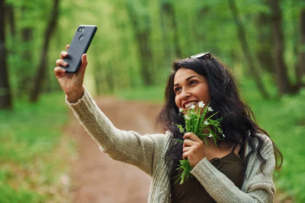 Morena Positiva Sosteniendo Flores Tomando Selfie Por Teléfono Bosque —  Fotos de Stock