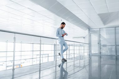 Gümüş renkli korkuluklara yaslanarak. Gündüz vakti ofiste resmi kıyafetler içinde genç yakışıklı bir adam..