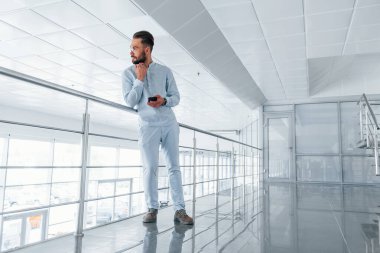 Gümüş renkli korkuluklara yaslanarak. Gündüz vakti ofiste resmi kıyafetler içinde genç yakışıklı bir adam..