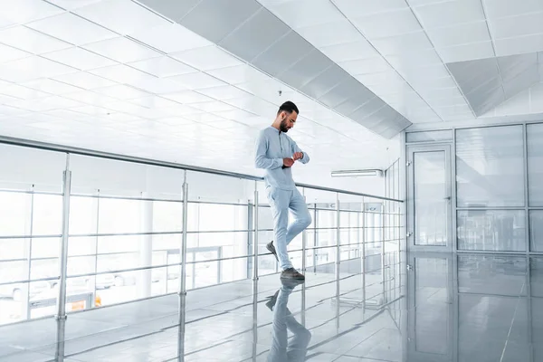 Gümüş renkli korkuluklara yaslanarak. Gündüz vakti ofiste resmi kıyafetler içinde genç yakışıklı bir adam..