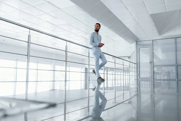 Gümüş renkli korkuluklara yaslanarak. Gündüz vakti ofiste resmi kıyafetler içinde genç yakışıklı bir adam..