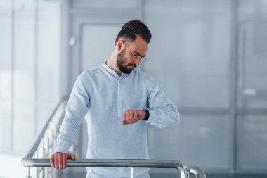 Gündüz vakti ofisteki gümüş renkli korkuluklara dayanan resmi giysili yakışıklı bir adamın ön görüntüsü..