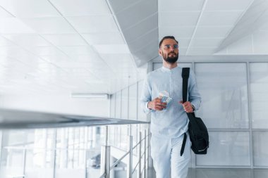 Elinde içki bardağı ve siyah çanta var. Gündüz vakti ofiste resmi kıyafetler içinde genç yakışıklı bir adam..