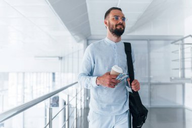 Elinde içki bardağı ve siyah çanta var. Gündüz vakti ofiste resmi kıyafetler içinde genç yakışıklı bir adam..