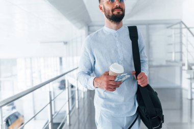 Elinde içki bardağı ve siyah çanta var. Gündüz vakti ofiste resmi kıyafetler içinde genç yakışıklı bir adam..