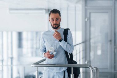 Elinde içki bardağı ve siyah çanta var. Gündüz vakti ofiste resmi kıyafetler içinde genç yakışıklı bir adam..