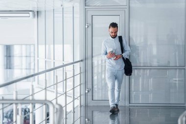 Elinde içki bardağı ve siyah çanta var. Gündüz vakti ofiste resmi kıyafetler içinde genç yakışıklı bir adam..