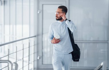 Elinde içki bardağı ve siyah çanta var. Gündüz vakti ofiste resmi kıyafetler içinde genç yakışıklı bir adam..