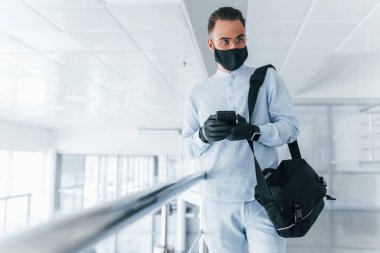 In protective mask and gloves. Young handsome man in formal clothes indoors in the office at daytime.