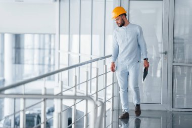 Gümüş renkli korkulukların yanında yürüyorum. Beyaz elbiseli ve turuncu koruyucu şapkalı mühendis içeride duruyor ve çalışıyor..