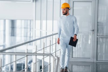 Gümüş renkli korkulukların yanında yürüyorum. Beyaz elbiseli ve turuncu koruyucu şapkalı mühendis içeride duruyor ve çalışıyor..