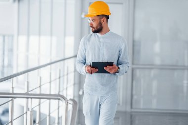 Gümüş renkli korkulukların yanında yürüyorum. Beyaz elbiseli ve turuncu koruyucu şapkalı mühendis içeride duruyor ve çalışıyor..