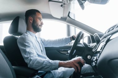 Gıcır gıcır yeni bir otomobilde oturan resmi kıyafetli genç adamın yan görüntüsü..
