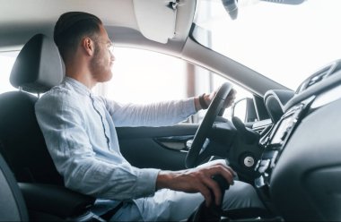 Gıcır gıcır yeni bir otomobilde oturan resmi kıyafetli genç adamın yan görüntüsü..