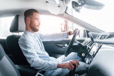 Gıcır gıcır yeni bir otomobilde oturan resmi kıyafetli genç adamın yan görüntüsü..