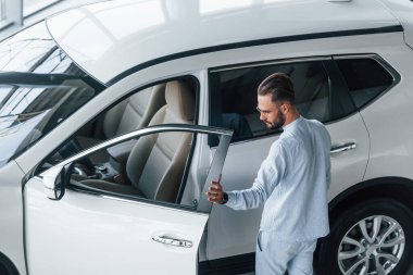 Beyaz elbiseli genç, zarif bir adam beyaz otomobilin yanında duruyor..