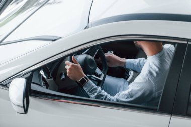 Gıcır gıcır giyinmiş genç bir adam yepyeni bir arabada oturuyor..