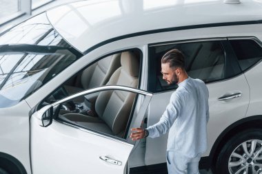 Beyaz elbiseli genç, zarif bir adam beyaz otomobilin yanında duruyor..