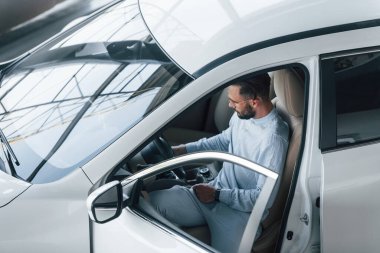 Gıcır gıcır giyinmiş genç bir adam yepyeni bir arabada oturuyor..