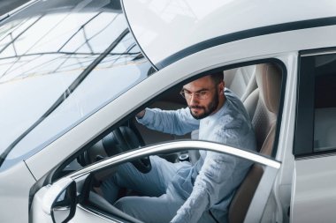 Gıcır gıcır giyinmiş genç bir adam yepyeni bir arabada oturuyor..