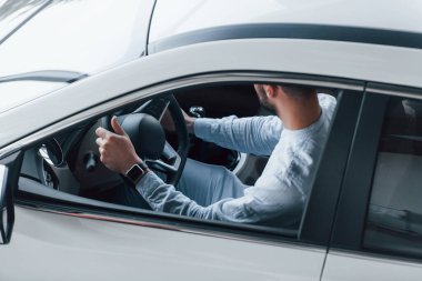 Gıcır gıcır giyinmiş genç bir adam yepyeni bir arabada oturuyor..