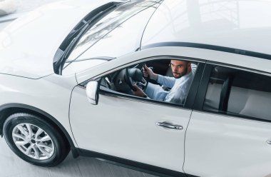 Gıcır gıcır giyinmiş genç bir adam yepyeni bir arabada oturuyor..