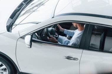 Gıcır gıcır giyinmiş genç bir adam yepyeni bir arabada oturuyor..