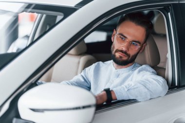 Gıcır gıcır yeni bir otomobilde oturan resmi kıyafetli genç adamın yan görüntüsü..