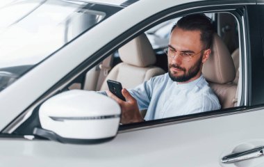 Gıcır gıcır yeni bir otomobilde oturan resmi kıyafetli genç adamın yan görüntüsü..