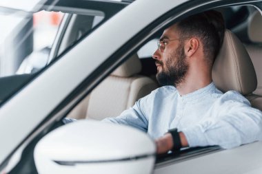 Gıcır gıcır yeni bir otomobilde oturan resmi kıyafetli genç adamın yan görüntüsü..