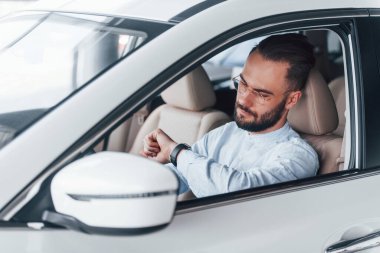 Gıcır gıcır yeni bir otomobilde oturan resmi kıyafetli genç adamın yan görüntüsü..