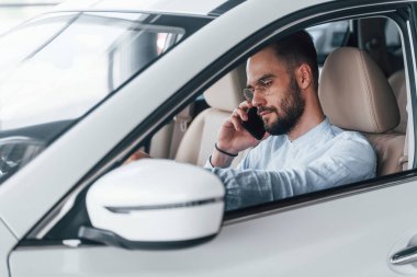 Gıcır gıcır yeni bir otomobilde oturan resmi kıyafetli genç adamın yan görüntüsü..