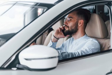 Gıcır gıcır yeni bir otomobilde oturan resmi kıyafetli genç adamın yan görüntüsü..