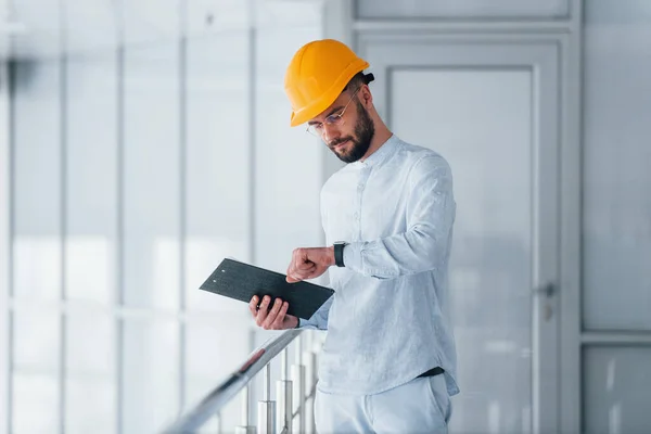 メモ帳を持ってる 白い服とオレンジ保護ハード帽子立って屋内で働くエンジニア — ストック写真