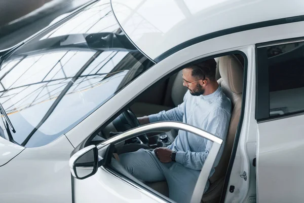 Gıcır gıcır giyinmiş genç bir adam yepyeni bir arabada oturuyor..