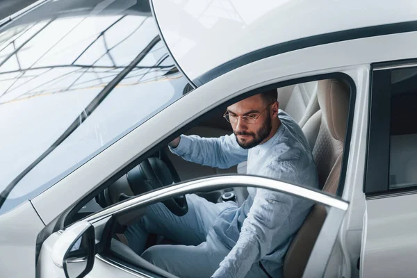 Gıcır gıcır giyinmiş genç bir adam yepyeni bir arabada oturuyor..