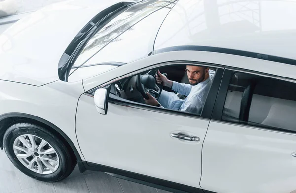 Gıcır gıcır giyinmiş genç bir adam yepyeni bir arabada oturuyor..