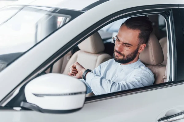 Gıcır gıcır yeni bir otomobilde oturan resmi kıyafetli genç adamın yan görüntüsü..