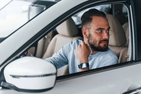Gıcır gıcır yeni bir otomobilde oturan resmi kıyafetli genç adamın yan görüntüsü..