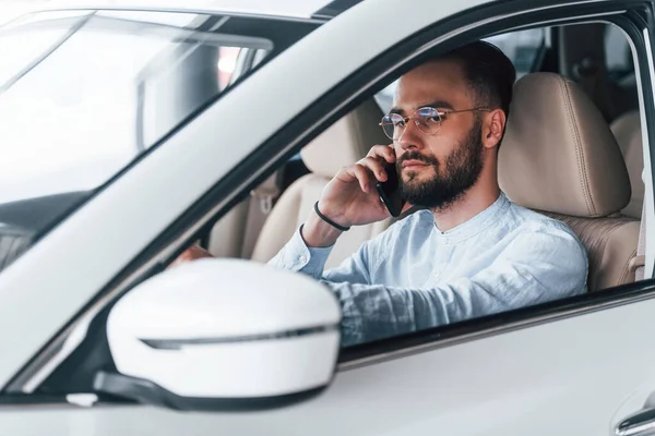 Gıcır gıcır yeni bir otomobilde oturan resmi kıyafetli genç adamın yan görüntüsü..