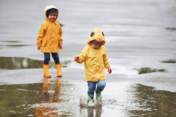 Two Kids Yellow Waterproof Cloaks Boots Playing Outdoors Rain Together — Stok fotoğraf
