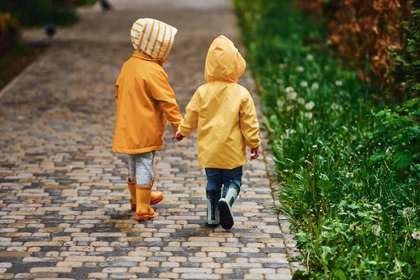 Two Kids Yellow Waterproof Cloaks Boots Holds Each Other Hands — Stock Photo, Image