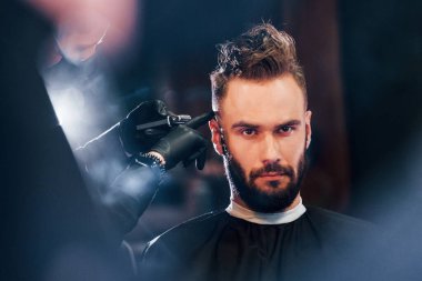 Genç sakallı adam berber dükkanında oturuyor ve saçını kestiriyor..