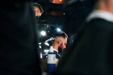 Genç sakallı adam berber dükkanında oturuyor ve saçını kestiriyor..