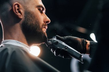 Şık bir saç stili olan genç adam berber dükkanında sakalını kestiriyor..