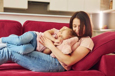 Kırmızı kanepede uzanıyordum. Genç bir anne ve küçük kızı evde birlikte günlük kıyafetler giyiyorlar..