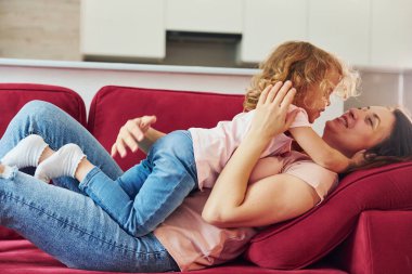 Kırmızı kanepede uzanıyordum. Genç bir anne ve küçük kızı evde birlikte günlük kıyafetler giyiyorlar..
