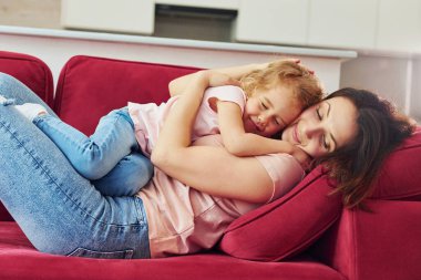 Kırmızı kanepede uzanıyordum. Genç bir anne ve küçük kızı evde birlikte günlük kıyafetler giyiyorlar..